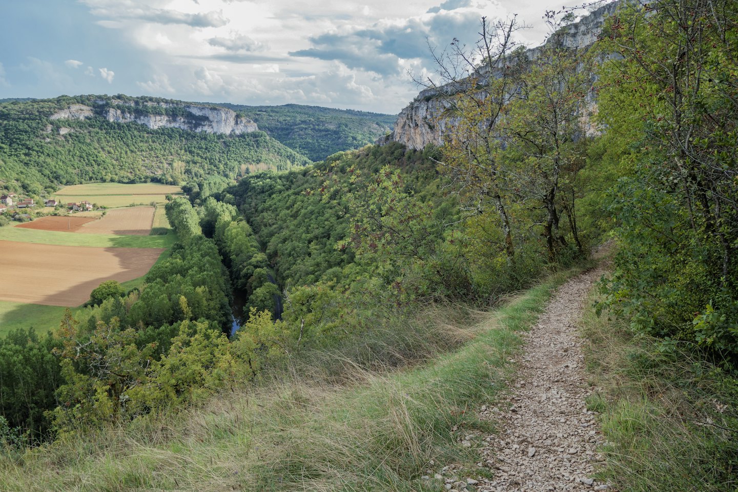 Vogelperspektive eines Tals mit Wanderweg, Wald, Klippen, Fluss und Dorf.